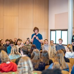 Leerlingen zitten in een zaal voor een workshop tijden de slotdag van De Inktaap in de Doelen in Rotterdam op 14 februari 2023. Eén van de leerlingen staat en spreekt in een microfoon.